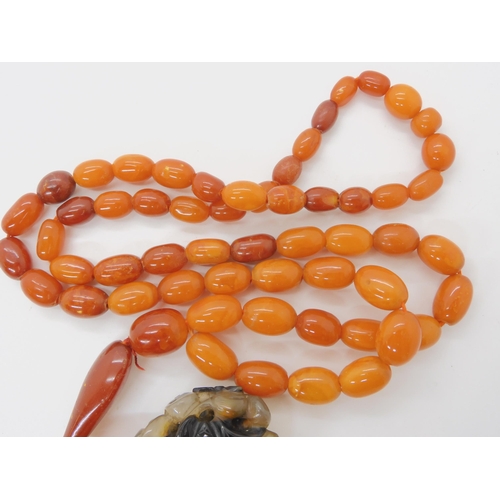 560 - A STRING OF AMBER BEADS WITH A CHINESE CARVED PENDANT