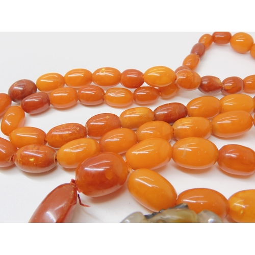 560 - A STRING OF AMBER BEADS WITH A CHINESE CARVED PENDANT