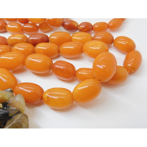 560 - A STRING OF AMBER BEADS WITH A CHINESE CARVED PENDANT