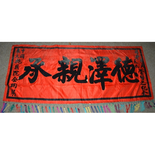 127 - A CHINESE SILK BANNER IN RED AND BLACK WITH CALLIGRAPHY