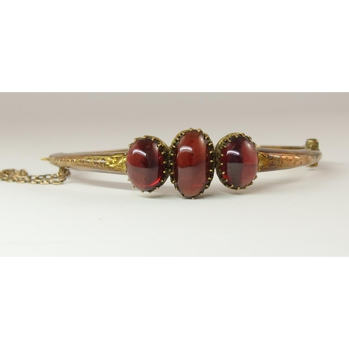 634 - A yellow metal bangle set with three garnet cabouchons