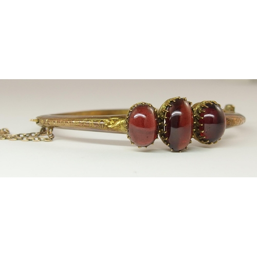 634 - A yellow metal bangle set with three garnet cabouchons