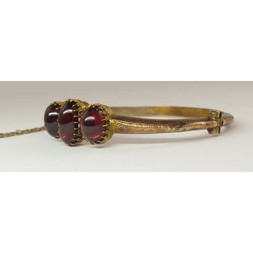 634 - A yellow metal bangle set with three garnet cabouchons