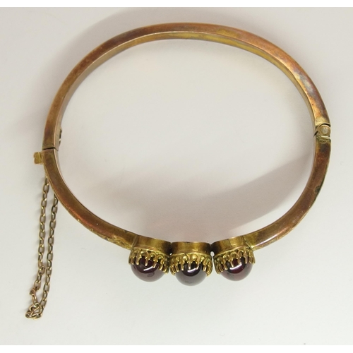 634 - A yellow metal bangle set with three garnet cabouchons