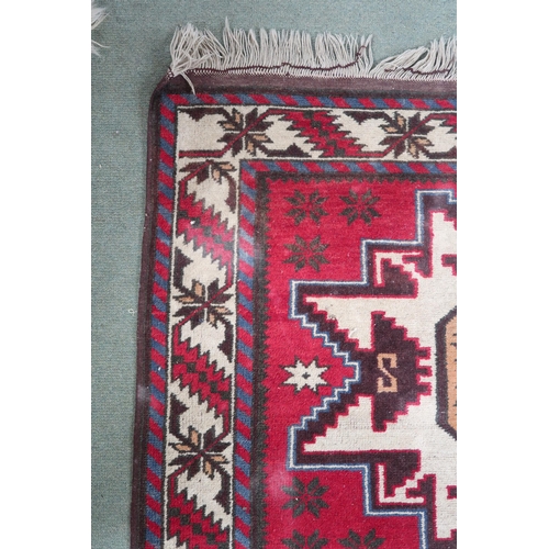 19 - A red ground Persian rug with three geometric medallions and cream borders, 191cm long x 104cm wide