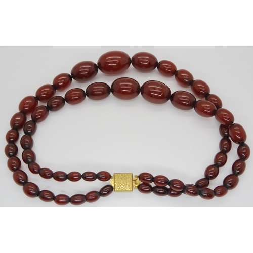 712 - A double string of cherry amber coloured beads, largest bead, 3cm x 2cm, shortest length approx 41.5... 