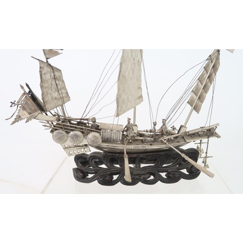 316A - A WHITE SILVER MODEL OF A JUNK mounted on a carved wood wave base, 20cm high, 22cm wide and 4cm... 