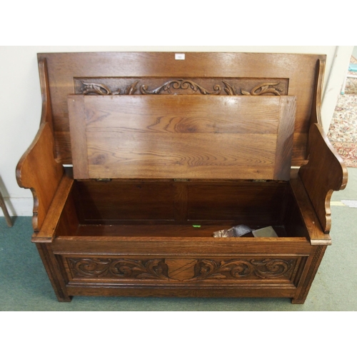 102 - An early 20th century oak monks bench/settle with carved back over hinged seat on base carved with f... 