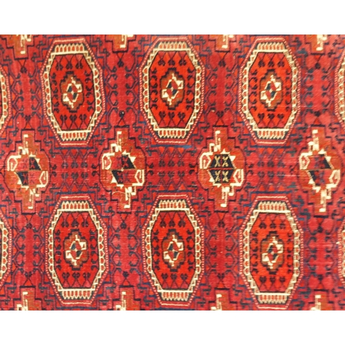 105 - A red ground Bokhara rug with all over medallion design and geometric borders