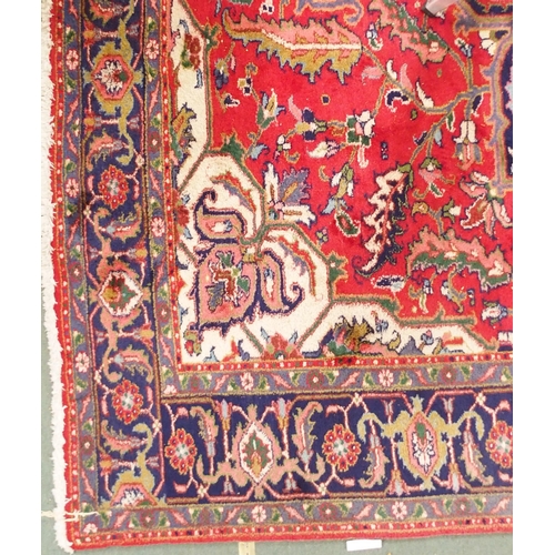 64 - A red ground Tabriz rug with multicoloured central medallion, matching spandrels and dark blue borde... 