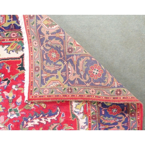 64 - A red ground Tabriz rug with multicoloured central medallion, matching spandrels and dark blue borde... 