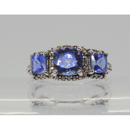 A 9ct white gold three stone cushion cut tanzanite ring with diamond accents, finger size J1/2, weight 2.3gms