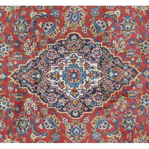 2142 - A RED GROUND KESHAN RUGwith all over floral foliate design, dark blue central medallion, matching sp... 