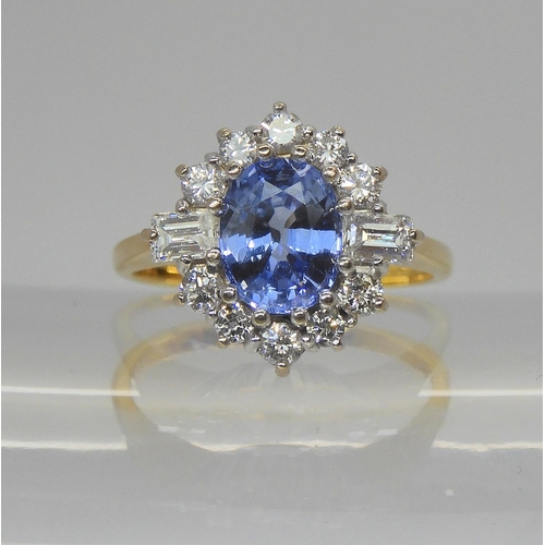 An 18ct yellow and white gold cornflower blue sapphire and diamond cluster ring, set with a 8mm x 6mm x 4mm sapphire, surrounded with baguette and brilliant cut diamonds, to an estimated approx diamond total of 0.66cts. Finger size M, weight 4.6gms