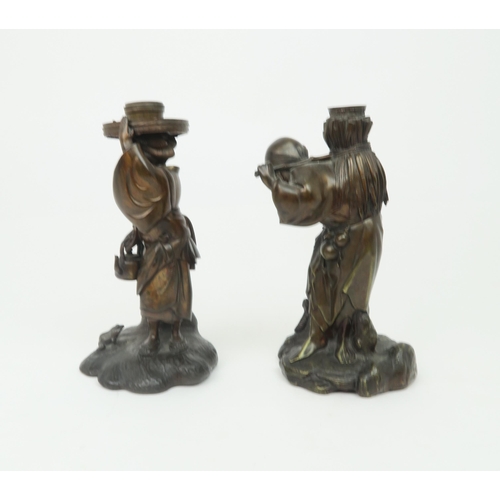 2354 - A PAIR OF JAPANESE BRONZE FIGURE CANDLESTICKSCast as a man carrying reeds and a woman carrying a ket... 