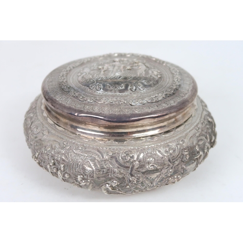 2410 - A BURMESE WHITE METAL CIRCULAR BOX AND COVER Cast with numerous figures and animals within foli... 