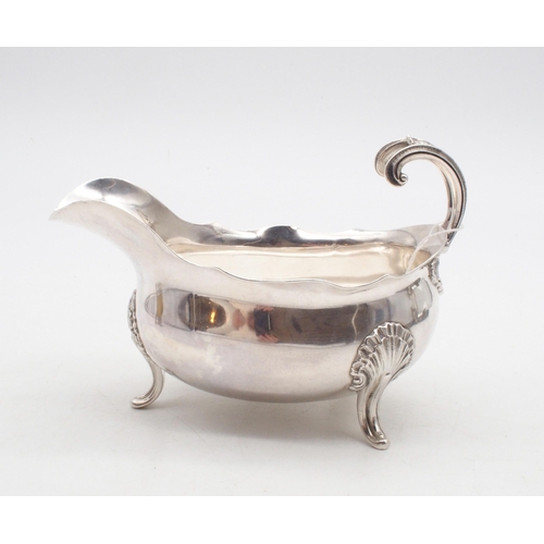 440 - A French silver sauce boat, with a shaped rim, a flying shell and scroll handle, supported on three ... 