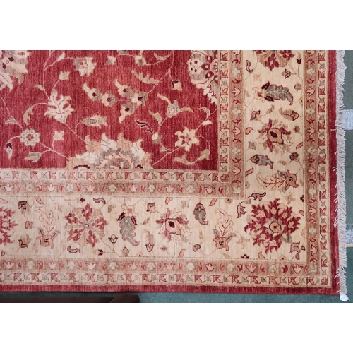 64 - A red ground Pakistani Zeigler rug with all-over floral design and cream flower head borders, 355cm ... 