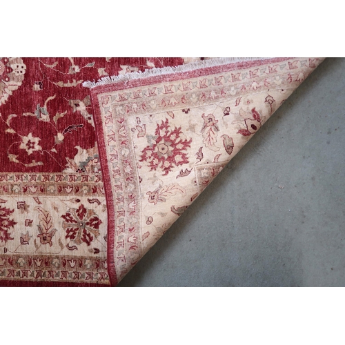 64 - A red ground Pakistani Zeigler rug with all-over floral design and cream flower head borders, 355cm ... 