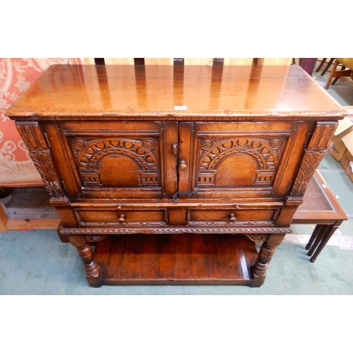 83 - A 20th century stained oak court cabinet with pair of carved cabinet doors over pair of drawers on t... 