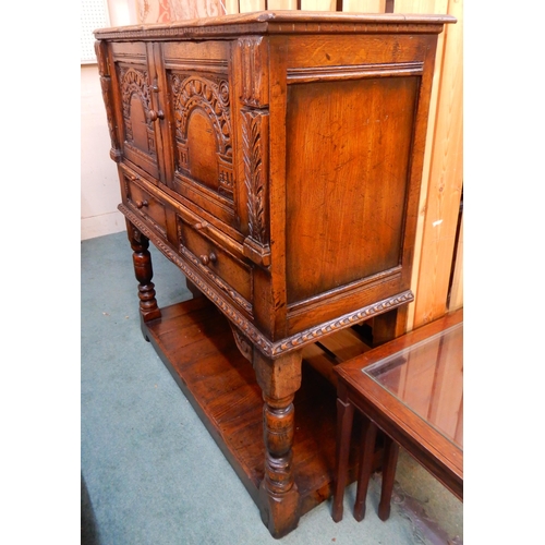 83 - A 20th century stained oak court cabinet with pair of carved cabinet doors over pair of drawers on t... 