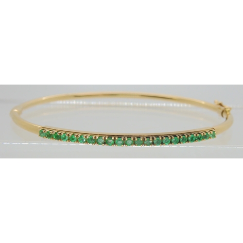 765 - A 14k gold bangle set with emeralds, inner dimensions 5.7cm x 5.2cm, weight 5.4gms