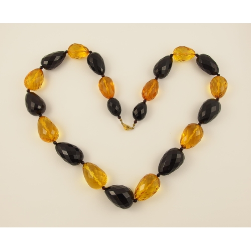 104 - Item 9. A long necklace of egg shaped yellow and dark cherry amber coloured beads