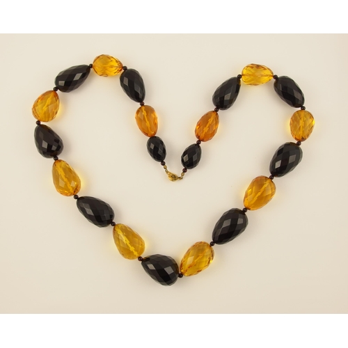 104 - Item 9. A long necklace of egg shaped yellow and dark cherry amber coloured beads