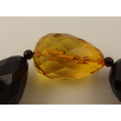 104 - Item 9. A long necklace of egg shaped yellow and dark cherry amber coloured beads