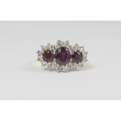 63 - A ruby and diamond cluster ring  set with an oval and two cushion cut rubies  surrounded with twenty... 