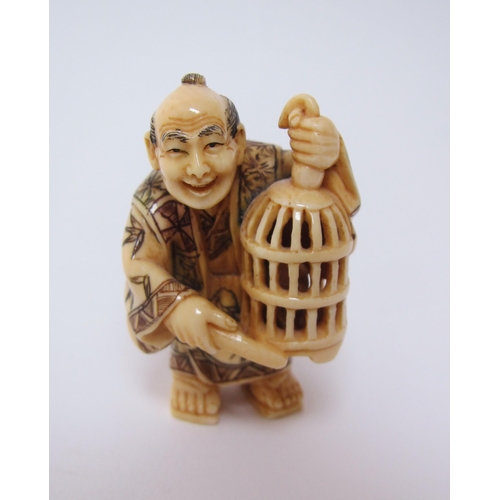 659 - A Japanese ivory netsuke of a man holding a bird cage and a stick