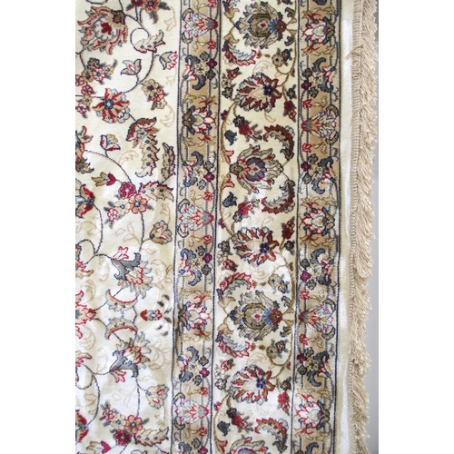 135 - A cream ground machine made Kashmiri rug with all-over floral design and flower head borders, 300cm ... 