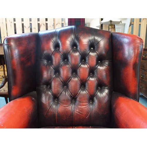 77 - A 20th century red leather button back upholstered Chesterfield style wing back armchair, 109cm high... 