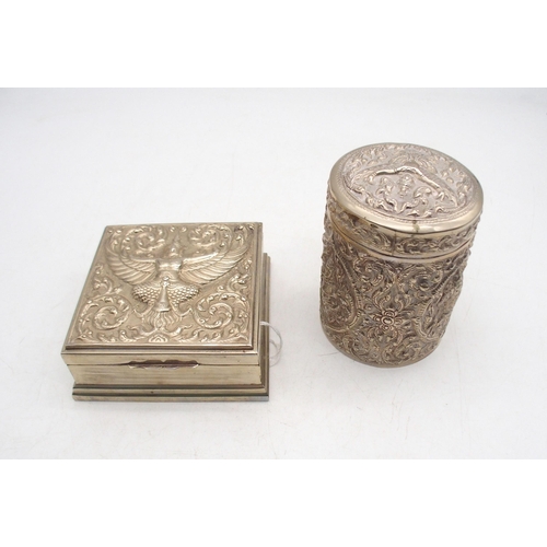 320 - Two Thai white metal boxes, both with embossed decoration of deities amongst flames, the cylindrical... 