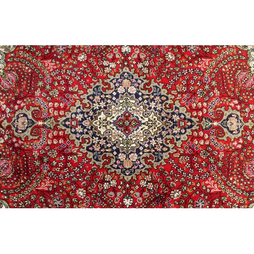 2135 - A RED GROUND TABRIZ RUGwith dark blue and cream central medallion, matching spandrels and a dark blu... 