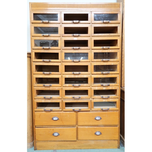 166 - An early 20th century blonde oak haberdashery cabinet with twenty four short glass front drawers ove... 