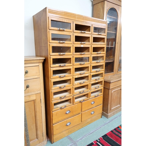 166 - An early 20th century blonde oak haberdashery cabinet with twenty four short glass front drawers ove... 