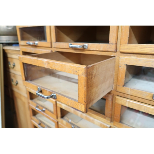 166 - An early 20th century blonde oak haberdashery cabinet with twenty four short glass front drawers ove... 