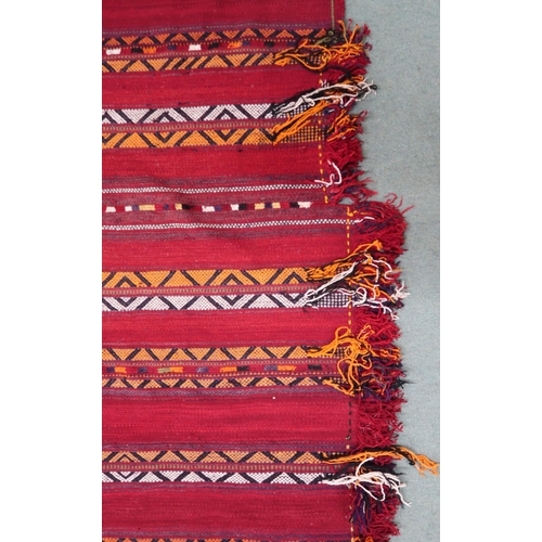 2142 - A RED GROUND MOROCCAN RUGwith multicoloured striped design, 298cm long x 196cm wide... 