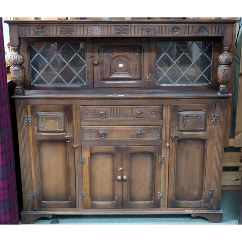 87 - A 20th century beech court style sideboard with inset cabinet door flanked by leaded glass panels ov... 