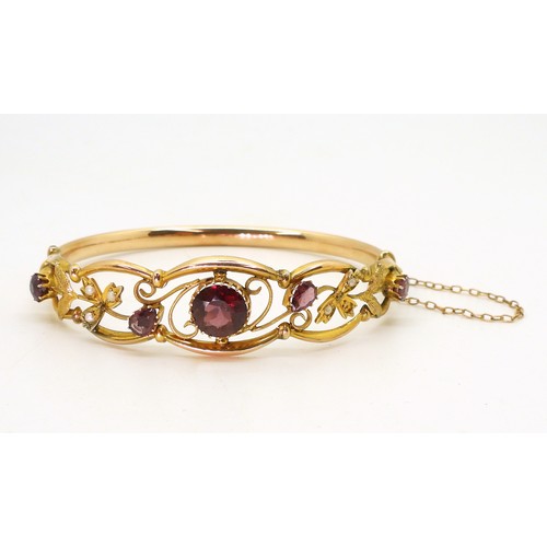 2852 - A VINTAGE FLORAL BANGLE set with round and pear shaped garnets and split pearls. Central garnet appr... 