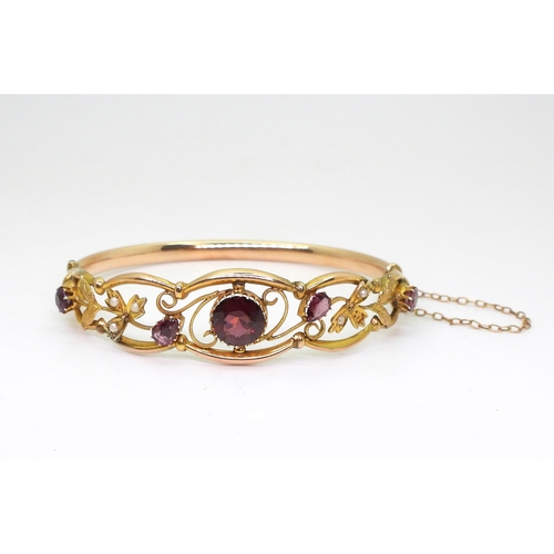 2852 - A VINTAGE FLORAL BANGLE set with round and pear shaped garnets and split pearls. Central garnet appr... 