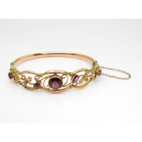 2852 - A VINTAGE FLORAL BANGLE set with round and pear shaped garnets and split pearls. Central garnet appr... 