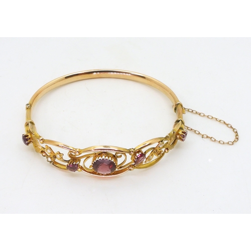 2852 - A VINTAGE FLORAL BANGLE set with round and pear shaped garnets and split pearls. Central garnet appr... 