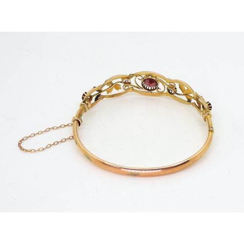 2852 - A VINTAGE FLORAL BANGLE set with round and pear shaped garnets and split pearls. Central garnet appr... 