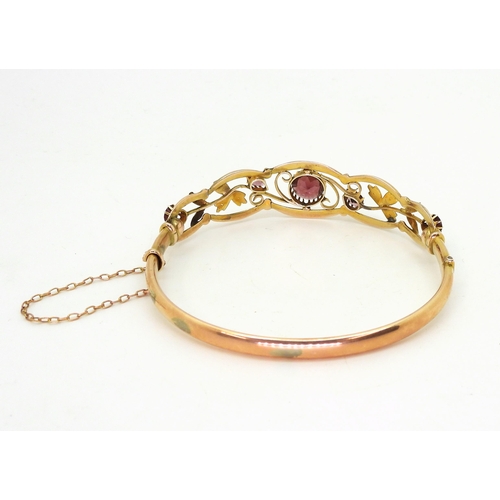 2852 - A VINTAGE FLORAL BANGLE set with round and pear shaped garnets and split pearls. Central garnet appr... 