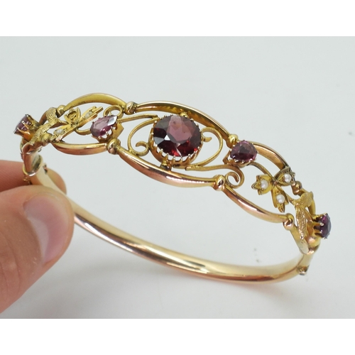 2852 - A VINTAGE FLORAL BANGLE set with round and pear shaped garnets and split pearls. Central garnet appr... 