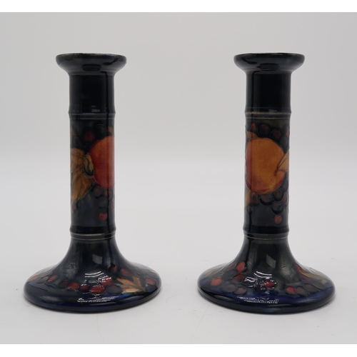 2158A - A PAIR OF MOORCROFT POMEGRANTE PATTERN CANDLESTICKSimpressed marks and signed in blue to base... 