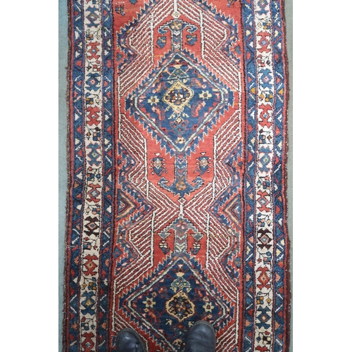 24 - A red ground tribal Hamadan runner with two geometric medallions and multicoloured borders, 232cm lo... 