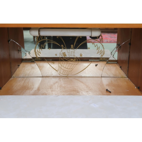 79 - A small mid 20th century teak drinks cabinet with fall front compartment with mirrored interior over... 